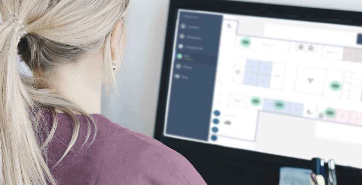 Healthcare professional reviewing a digital floor plan on a computer for patient monitoring and care coordination.