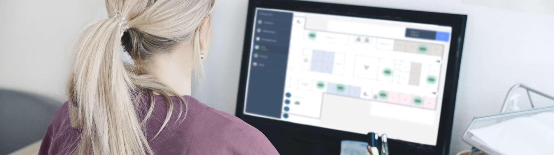 Healthcare professional reviewing a digital floor plan on a computer for patient monitoring and care coordination.