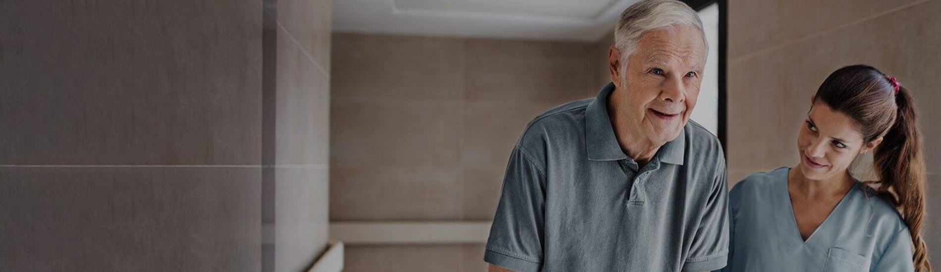 Old man assisted by a nurse walking down a corridor