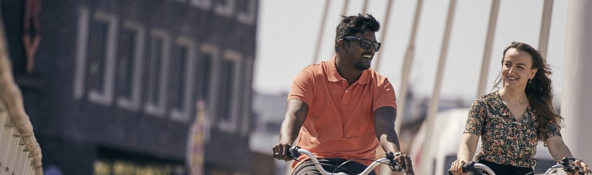Two people cycling side by side on a contemporary bridge in a city setting, enjoying outdoor activity